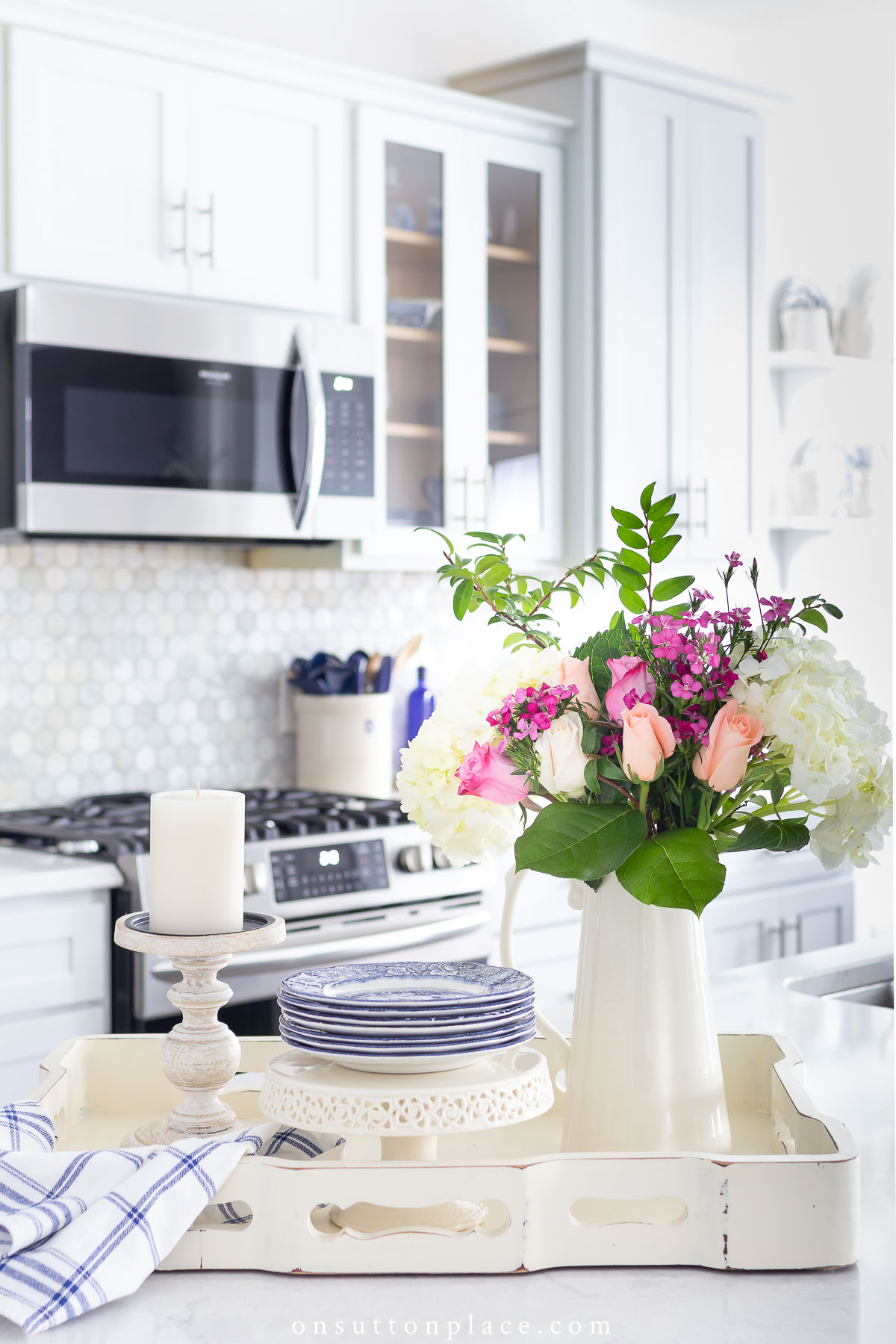 https://www.onsuttonplace.com/wp-content/uploads/2022/02/tray-with-flowers-plates-and-candle-on-kitchen-island.jpg